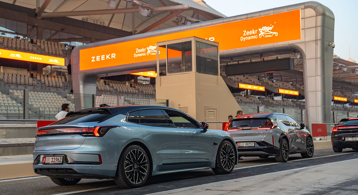 Sleek light blue Zeekr electric hatchback parked on a track paddock under a large orange Zeekr Dynamic arch